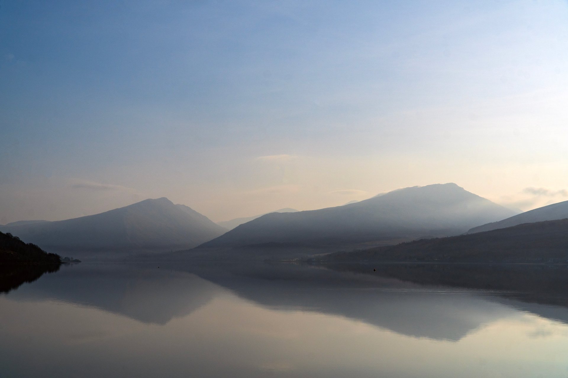 Three mountains reflected in calm lake water at dawn with misty atmosphere