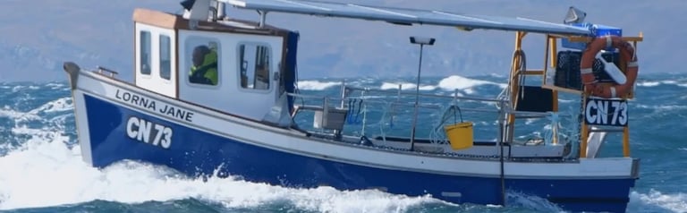 Blue and white fishing boat with registration number CW79 moving through rough ocean waves